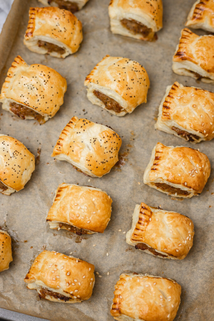 freshly baked sausage rolls on a lined baking tray.