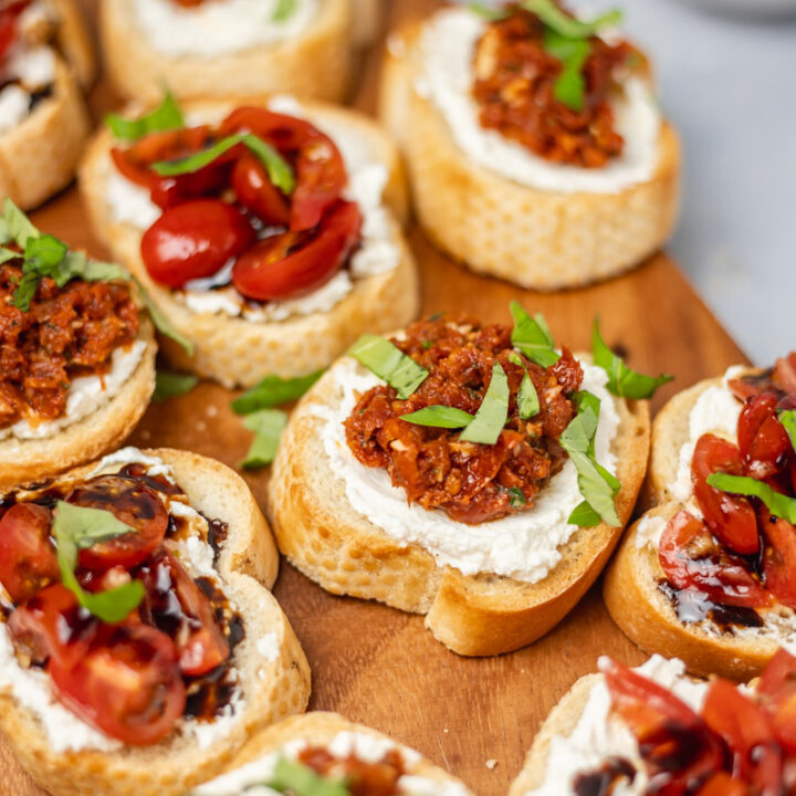 crostini topped with cream and tomatoes on a wooden platter.
