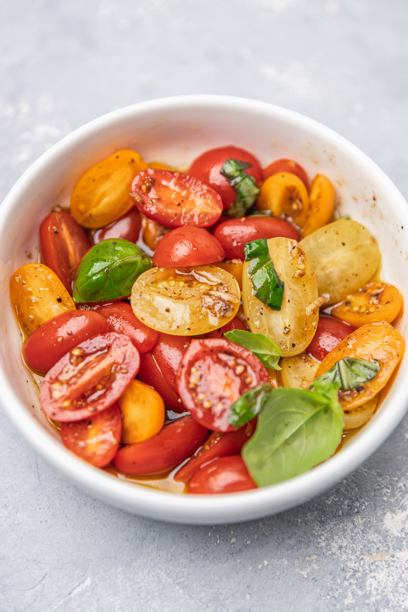 marinated tomatoes garnished with fresh basil leaves in a bowl.
