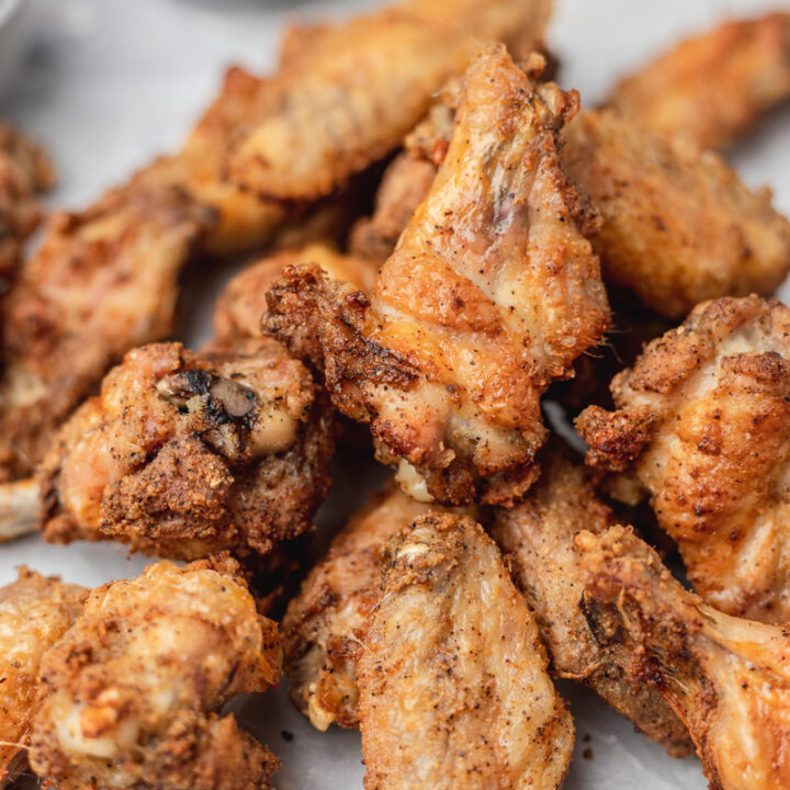 pile of crispy chicken wings on a parchment paper with a side of red dipping sauce.