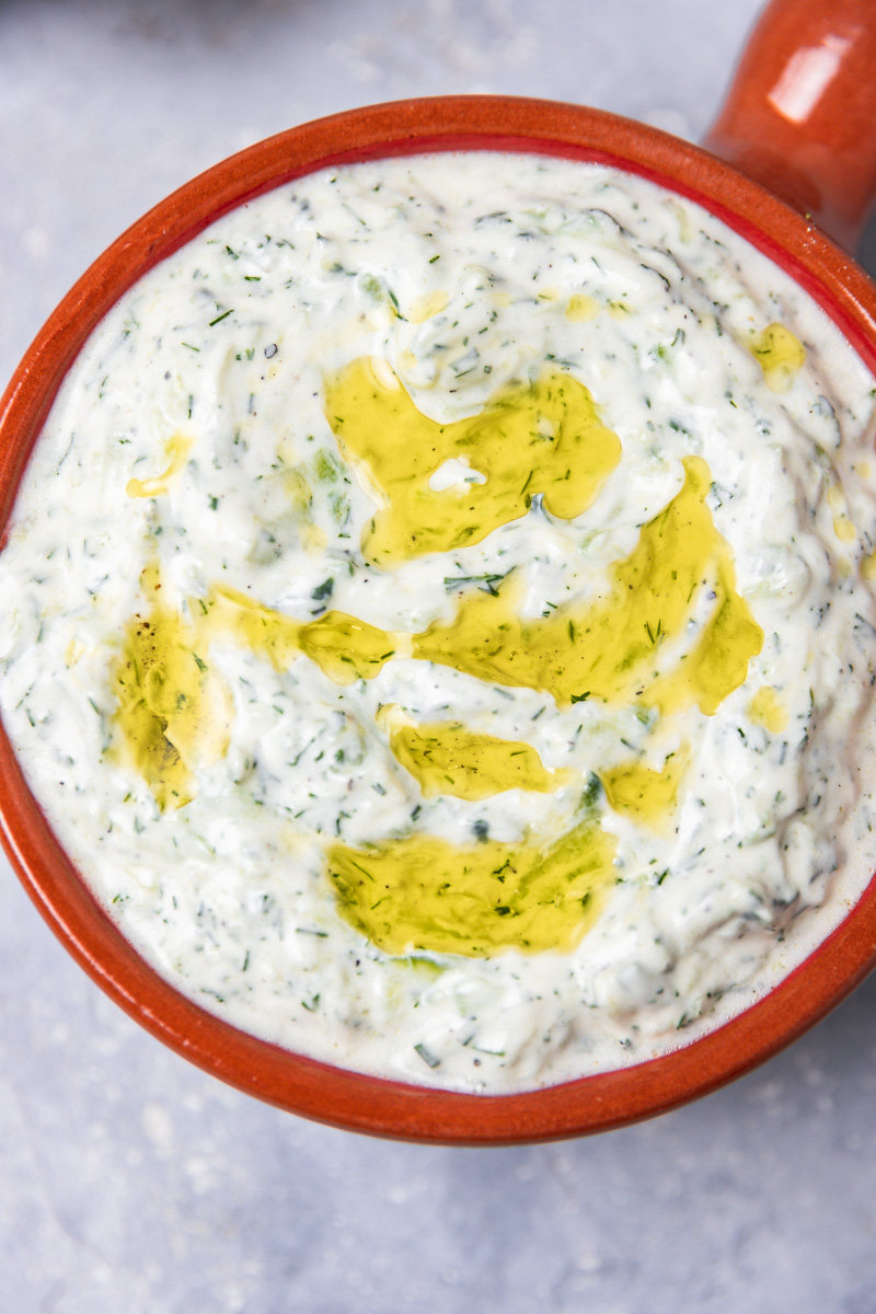 a close shot of a bowl of cucumber yogurt dip drizzed with olive oil.