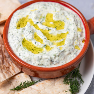 a bowl od cucumber yogurt dip an d pita bread.