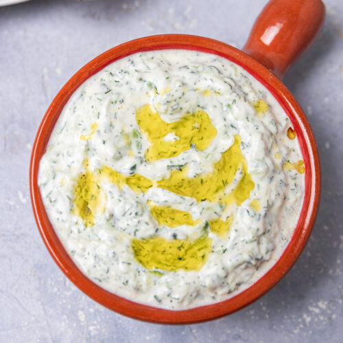 a bowl of yogurt-cucumber sauce placed beside fresh pita bread.