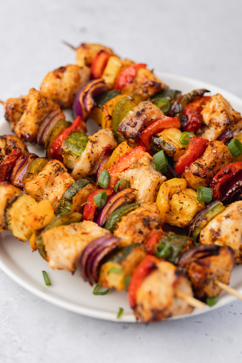 cooked chicken kabobs on a white plate garnished with chopped green onions.