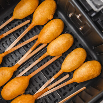 cooked mini corn dogs on sticks in air fryer basket.