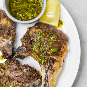 cooked lamb chops on a plate with lemon wedge.