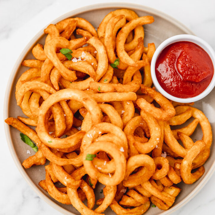 a plate of crispy curly fries and a small pot of ketchup.