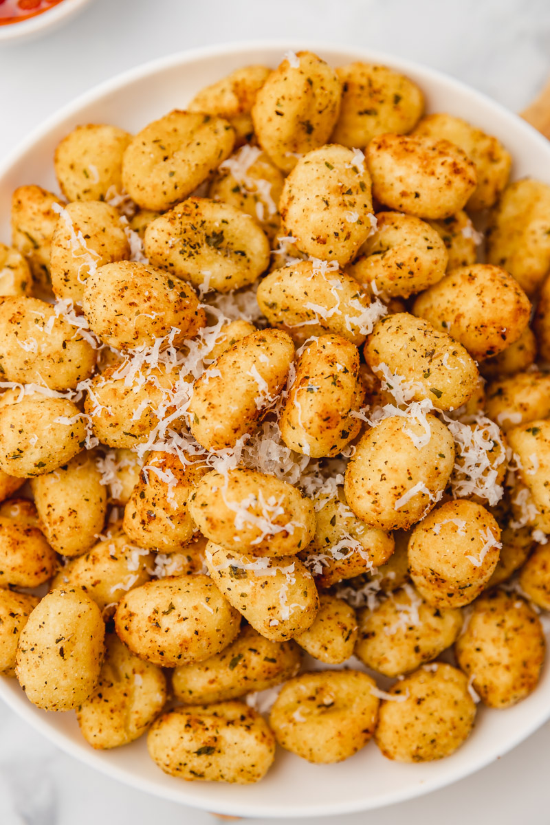 a plate of air fried seasoned golden brown gnocchi with grated parmesan cheese.