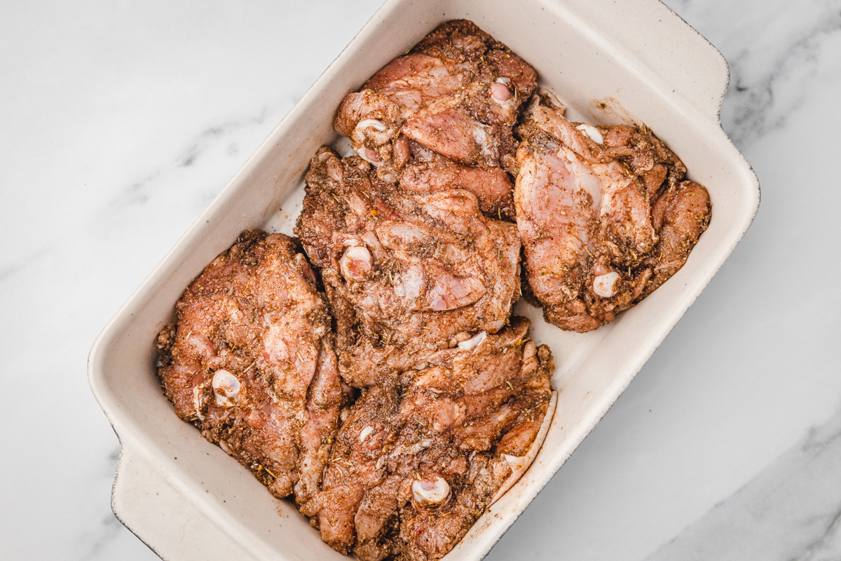 raw seasoned chicken thighs in a baking dish.