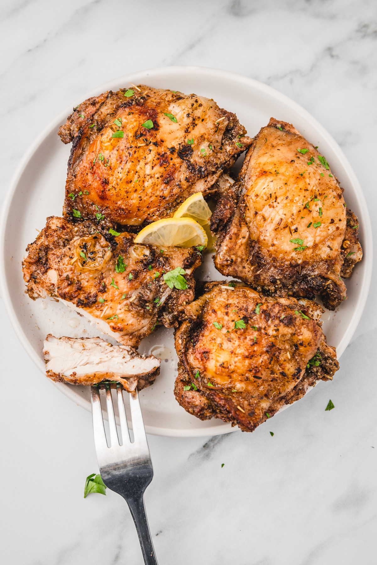 four chicken thighs with one of the chicken sliced into on a white plate.