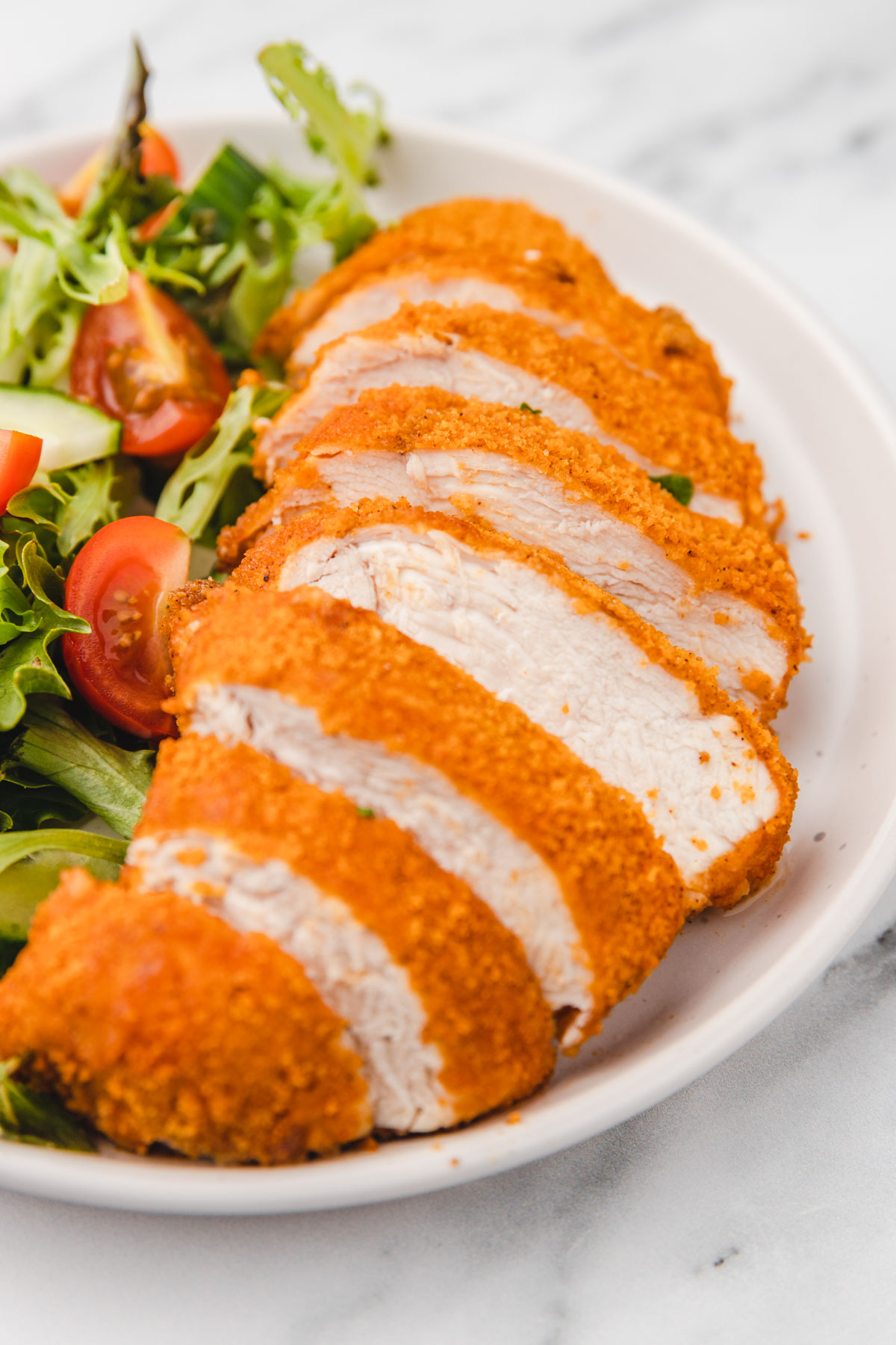 sliced chicken breast on a plate witha side of green salad.