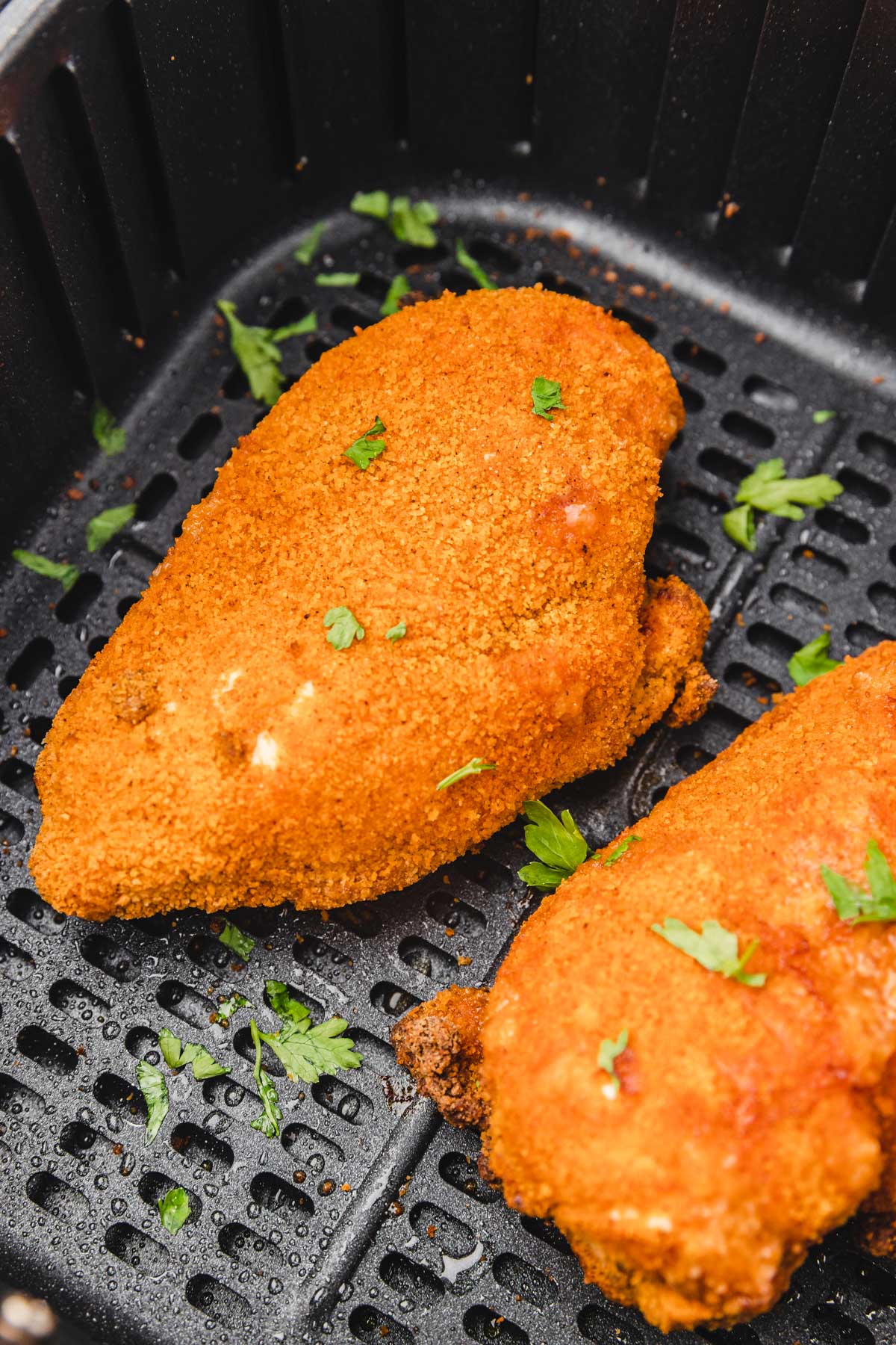 shake and bake chicken breast in an air fryer basket garnished with parsley.