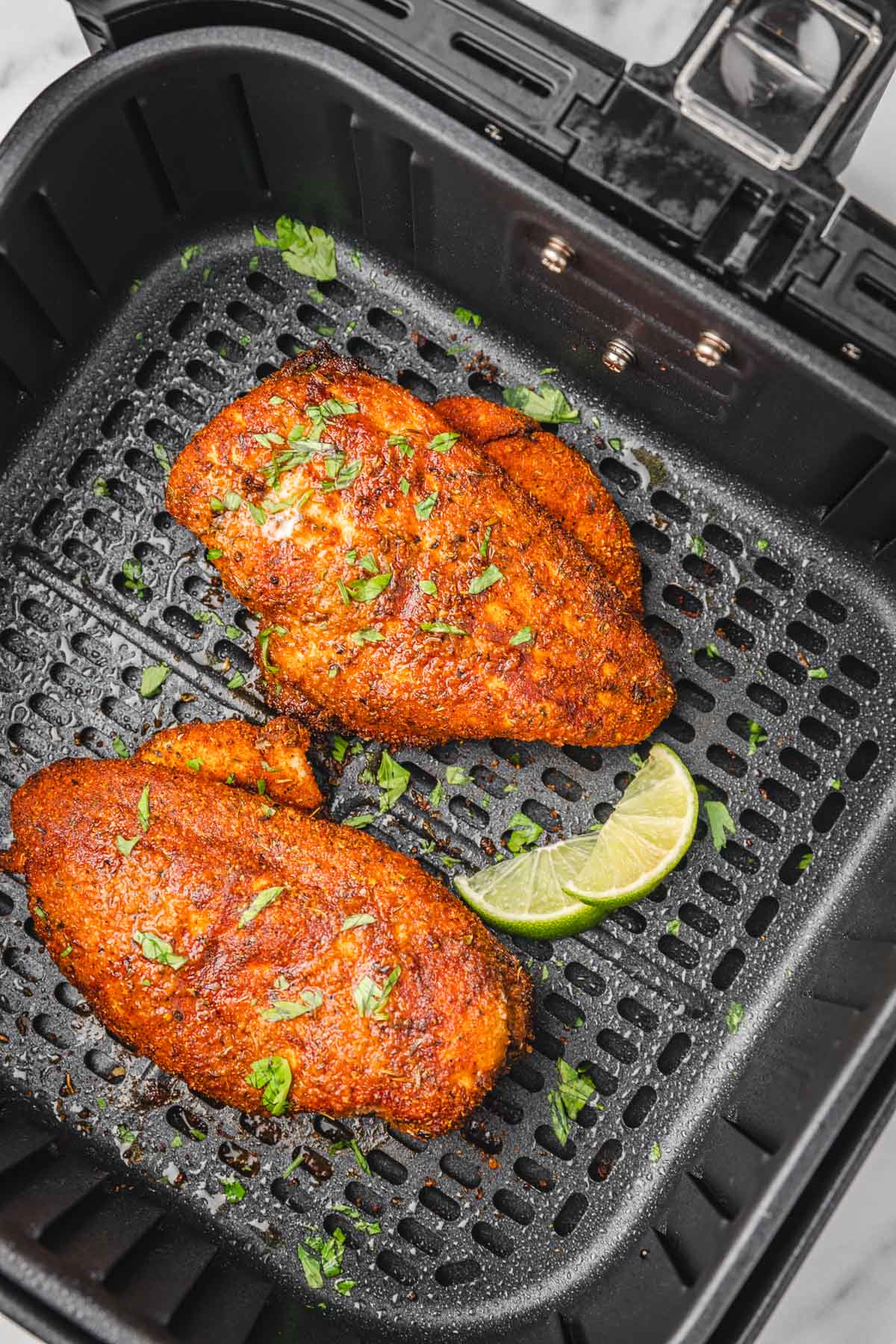 two blackened chicken breast in air fryer basket.