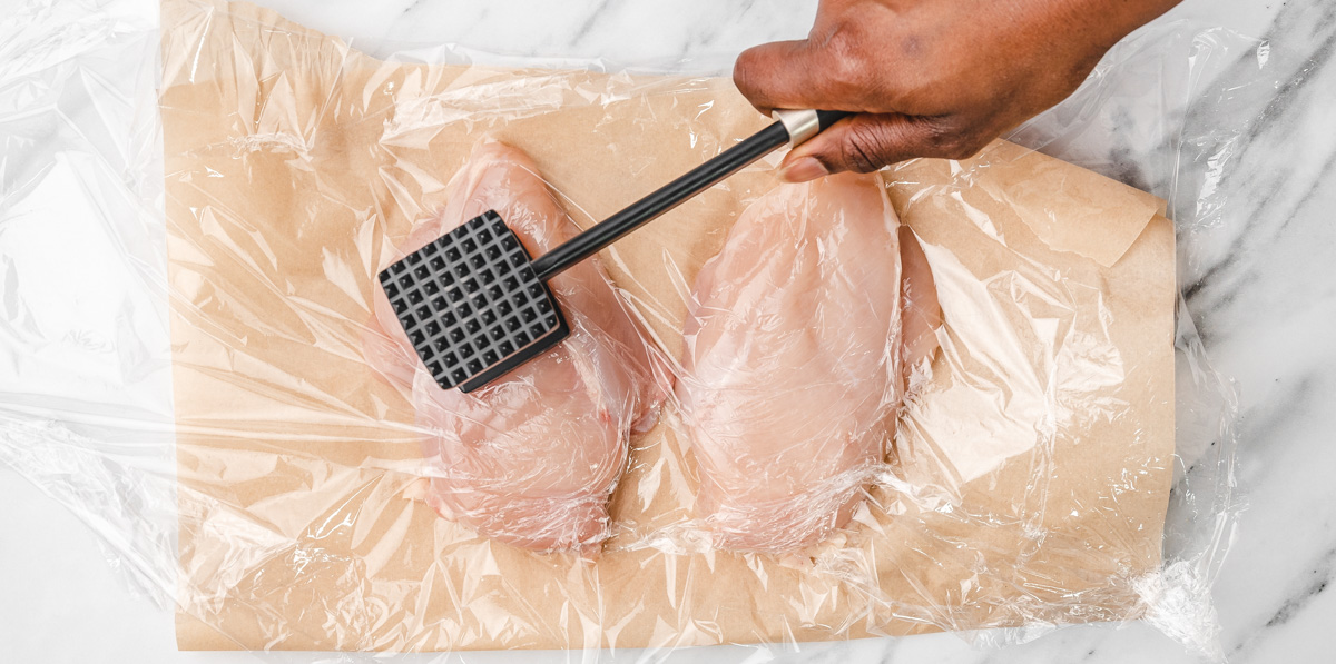 a hand flattening chicken breast with a mallet.
