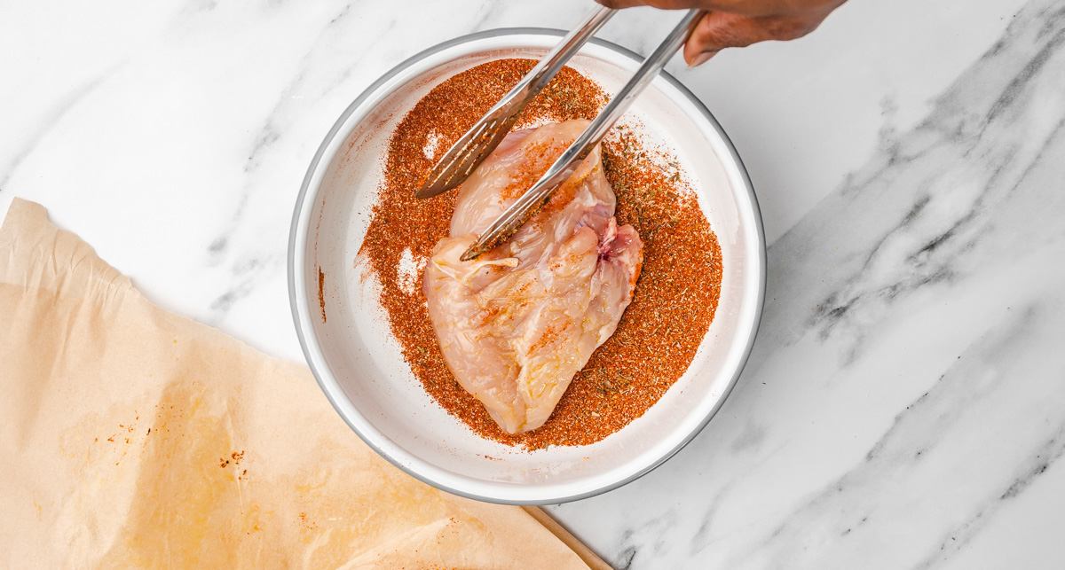 a hand pressing chicken breast into slice mix in a bowl.