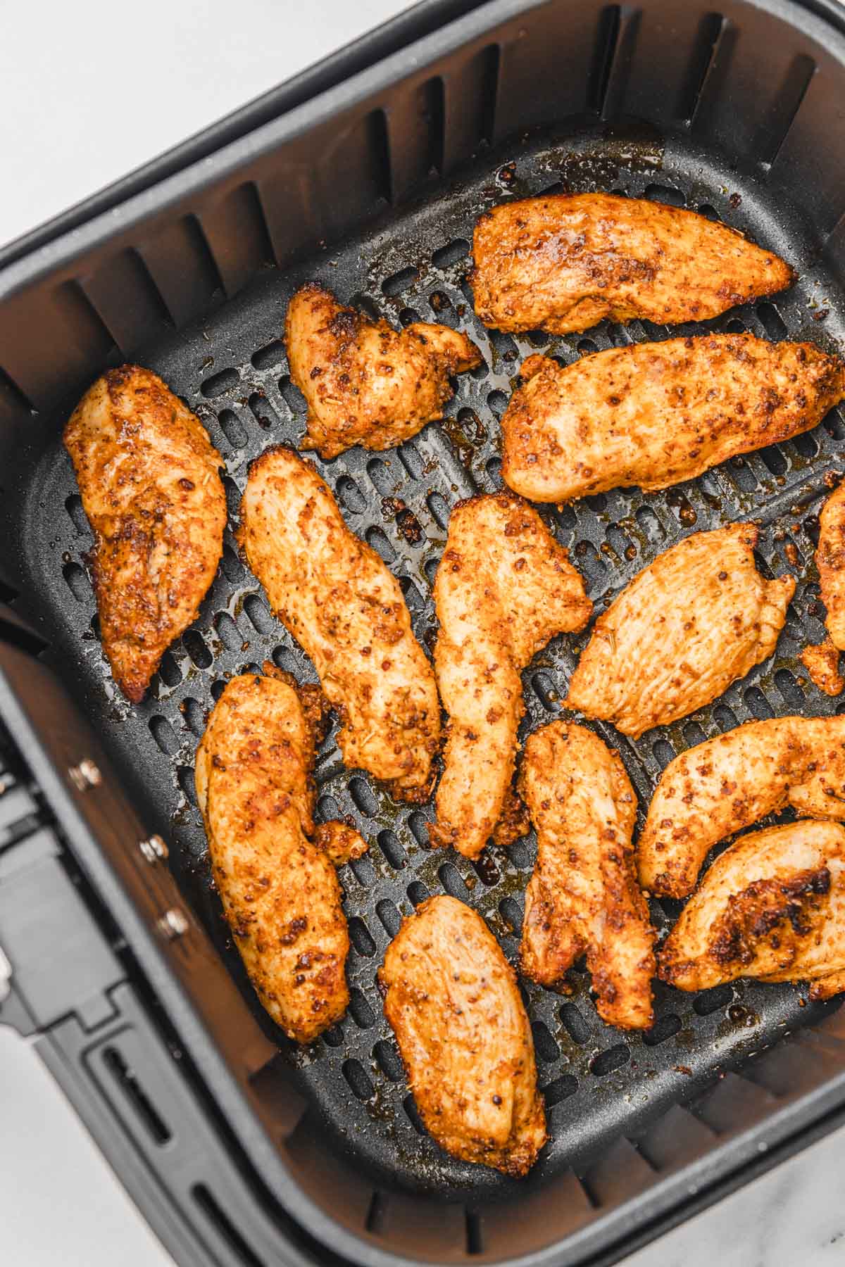 cooked unbreaded chicken strips in air fryer basket.