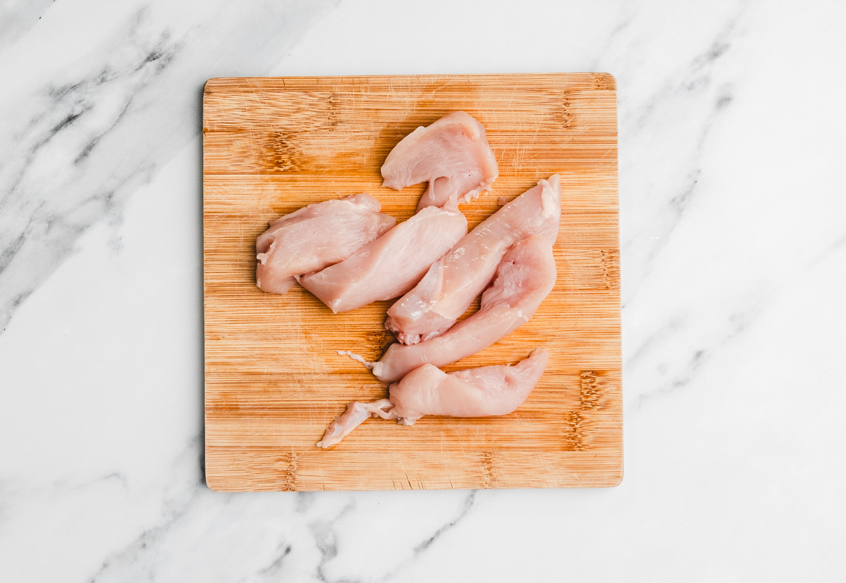 raw chicken strips on a chopping board.
