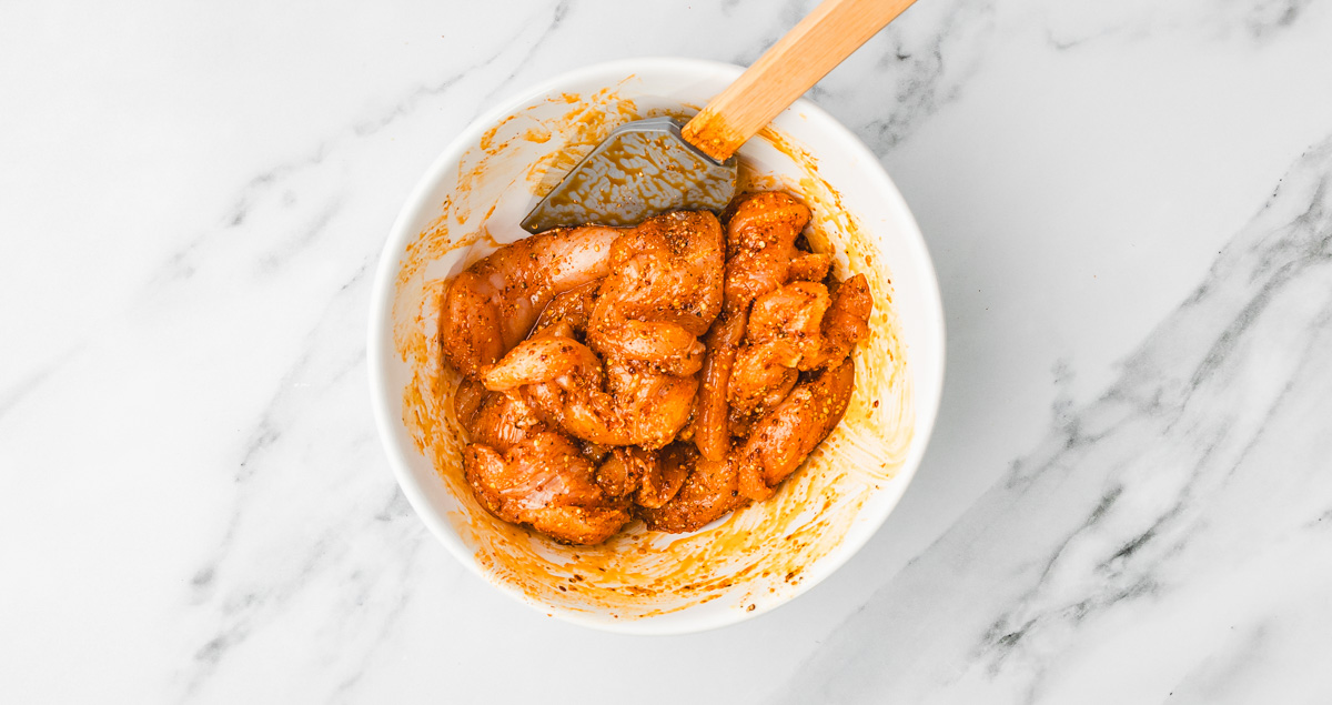 seasoned chicken strips in a white bowl with spatula.