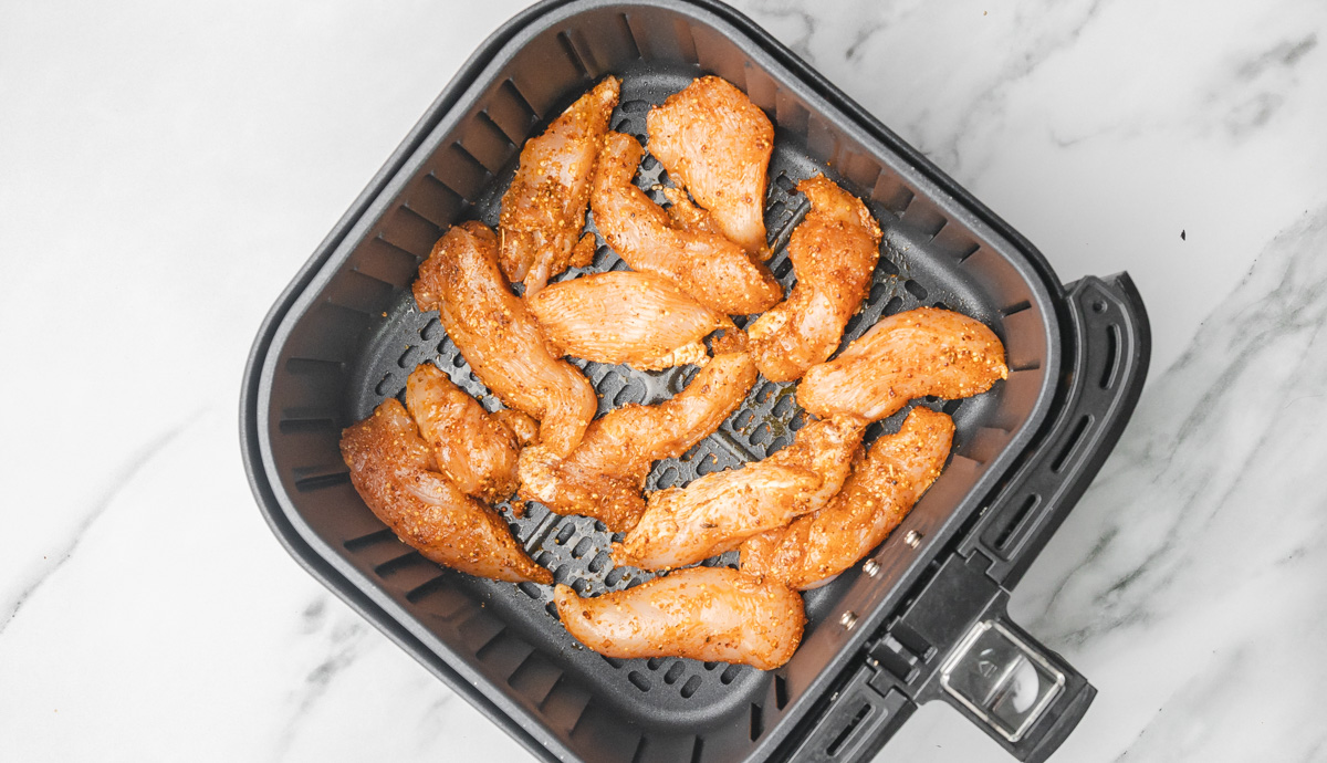 uncooked chicken strips in air fryer basket.