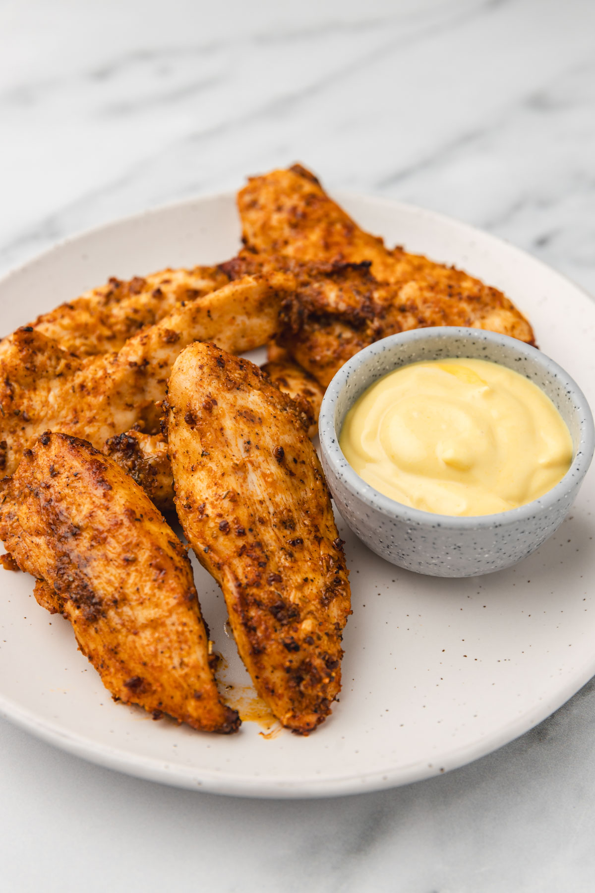 a plate of chicken strips with yellow dippig sauce in a dipping pot.