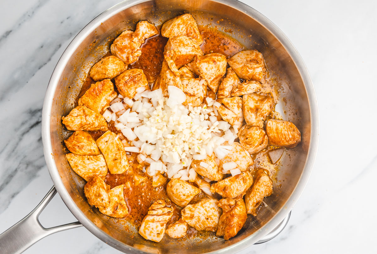 onions and garlic added to cubed chicken in askillet.