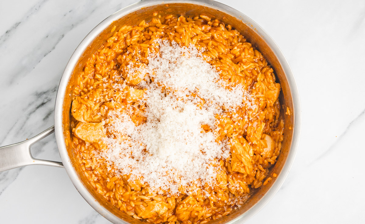 grated parmesan cheese added to pasta cooking on the stove.