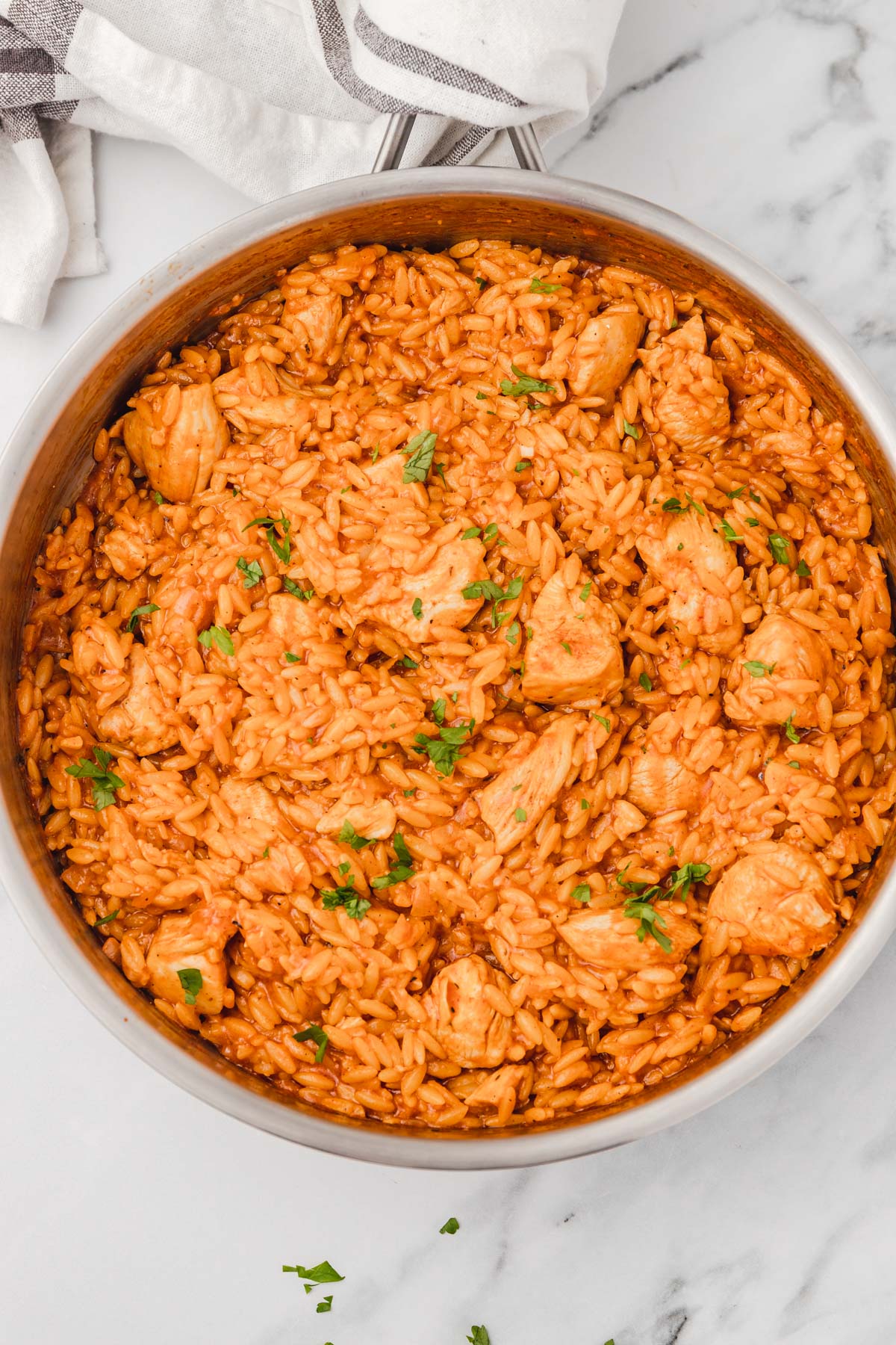 tomato chicken and orzo in a skillet garnished with chopped parsley.