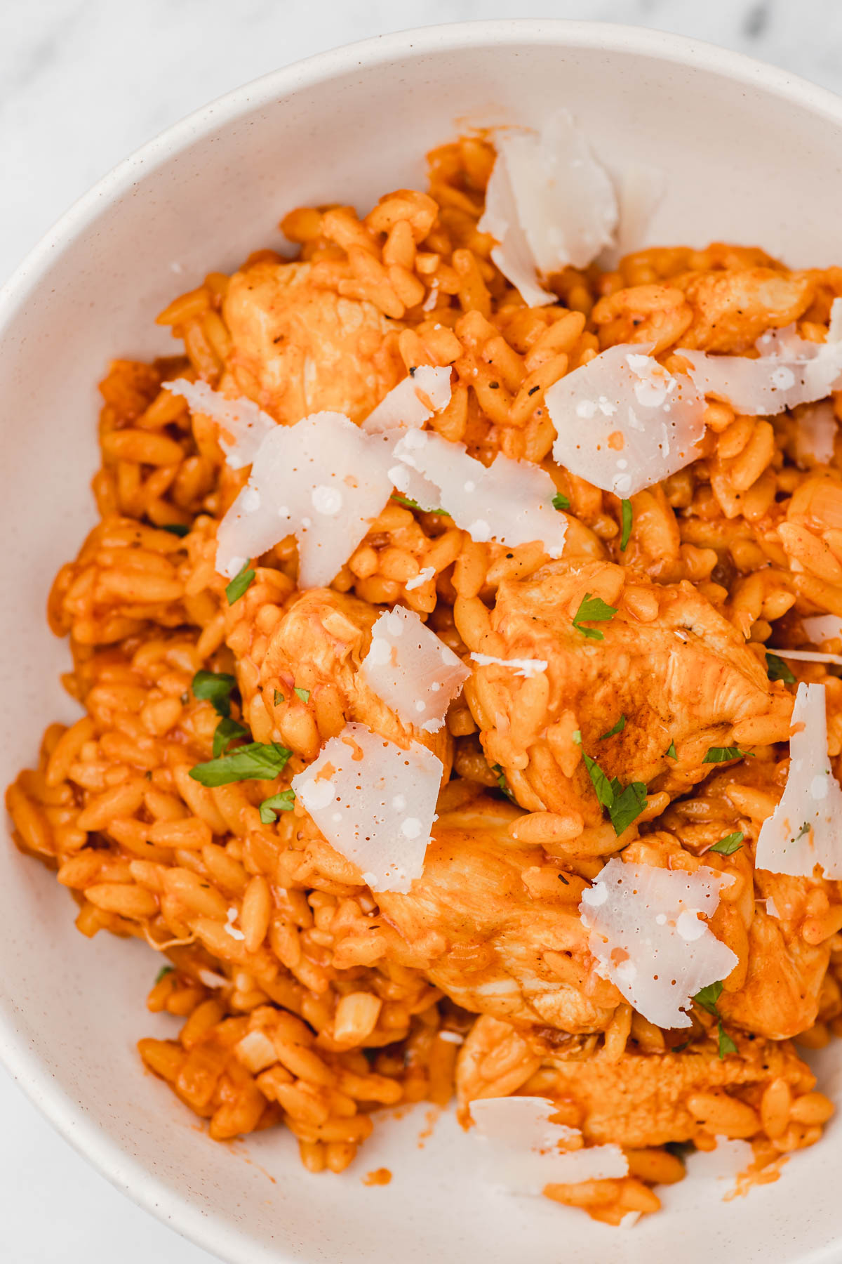 a bowl of cajun chicken orzo garnieshed with shaved parmesan cheese.