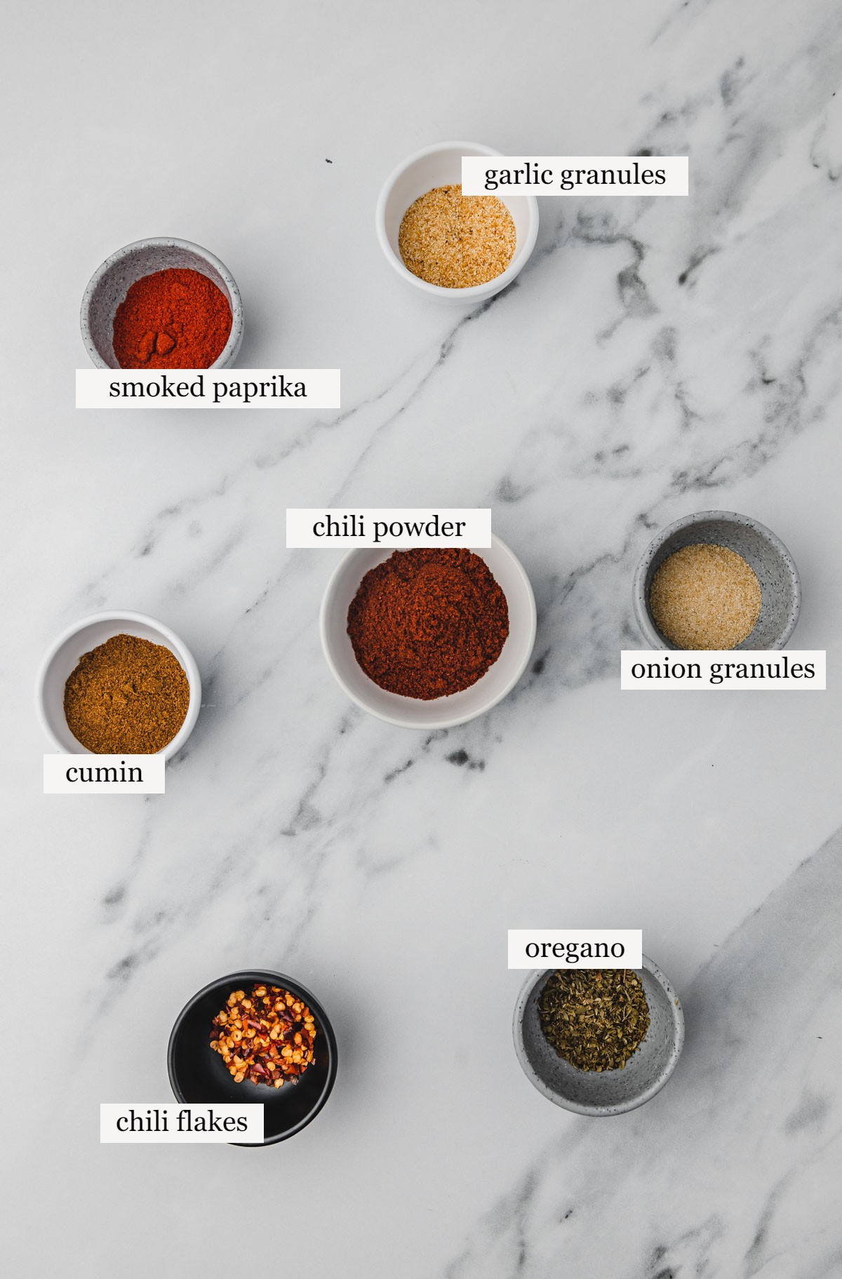 ingredients for taco seasoning on a white marble.