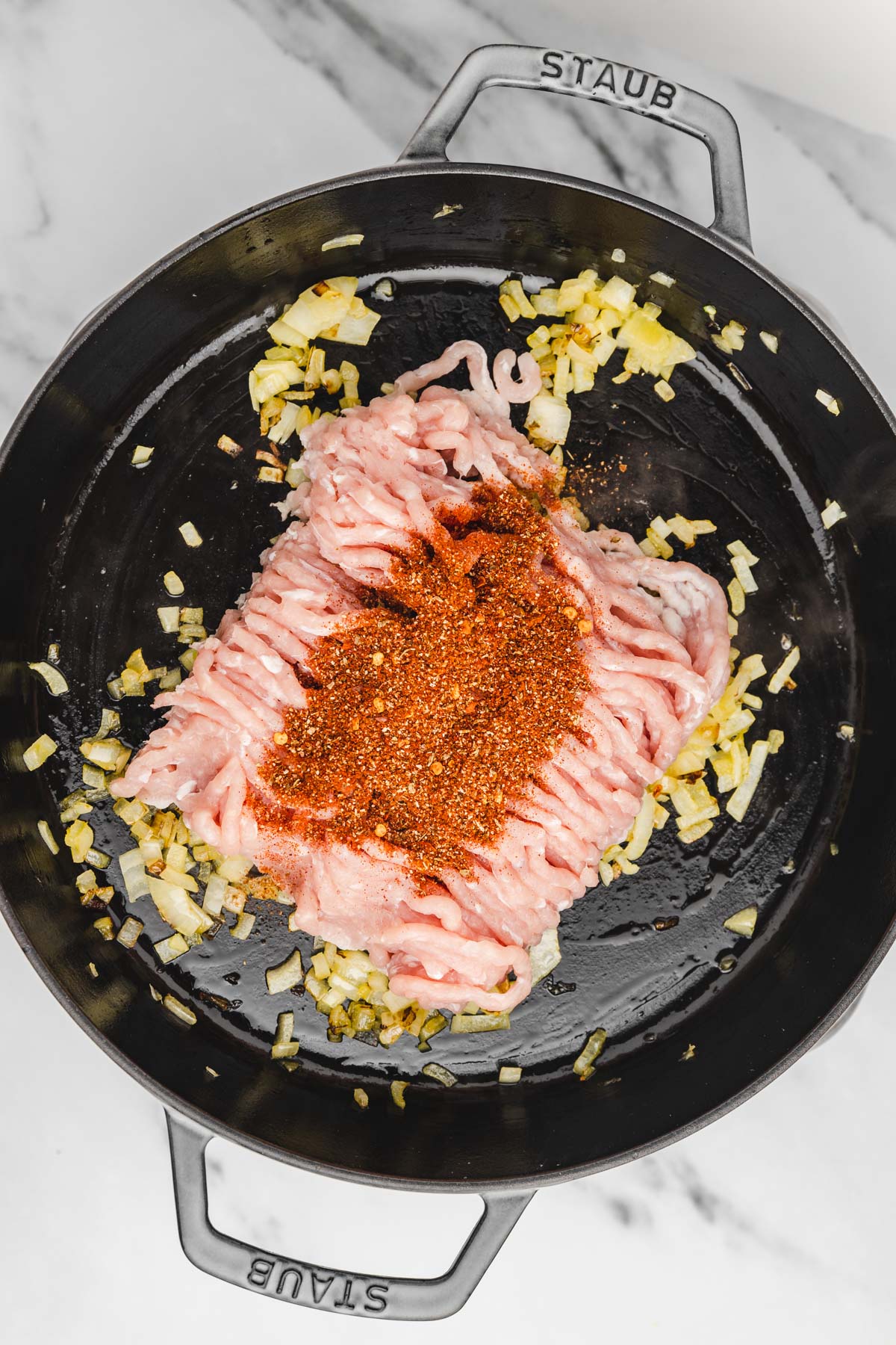 seasoning added to raw ground chicken in a cast iron.