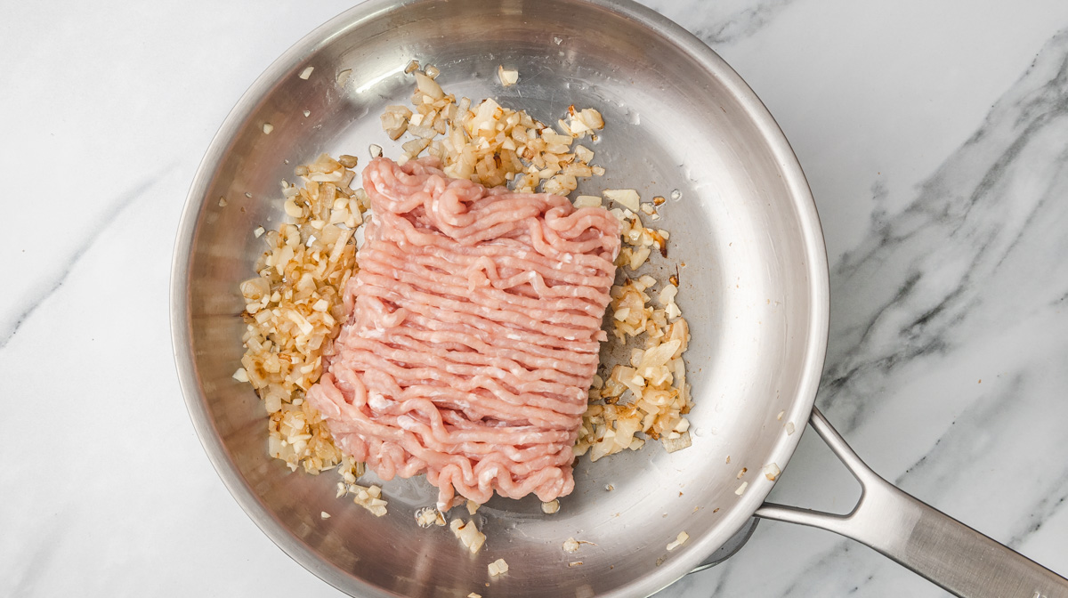 raw ground chicken in a skillet with sauteed onions and garlic.