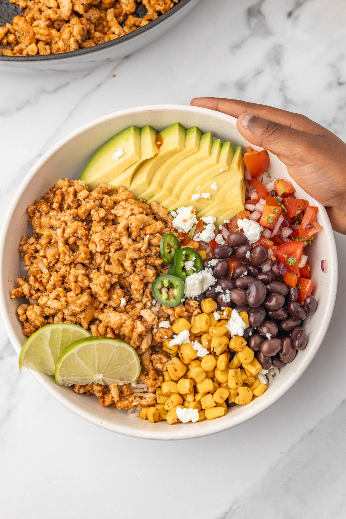 a hand holding a bowl of rice and chicken.