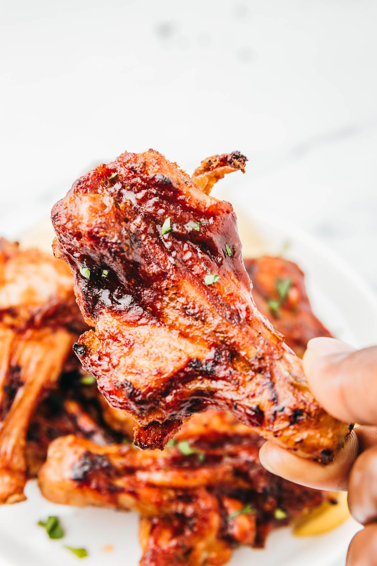 a hand holding bbq butterflied chiken drumstick.