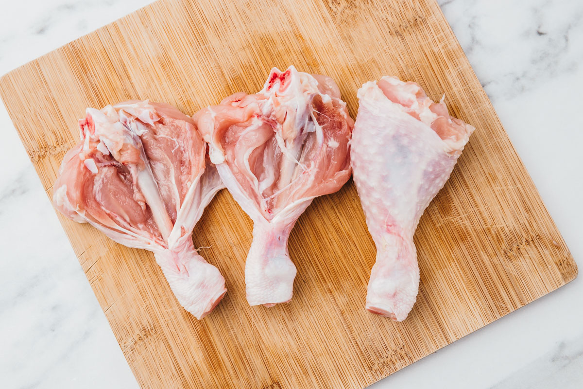 two butterflied chicken drumsticks with awole one on a chopping board.