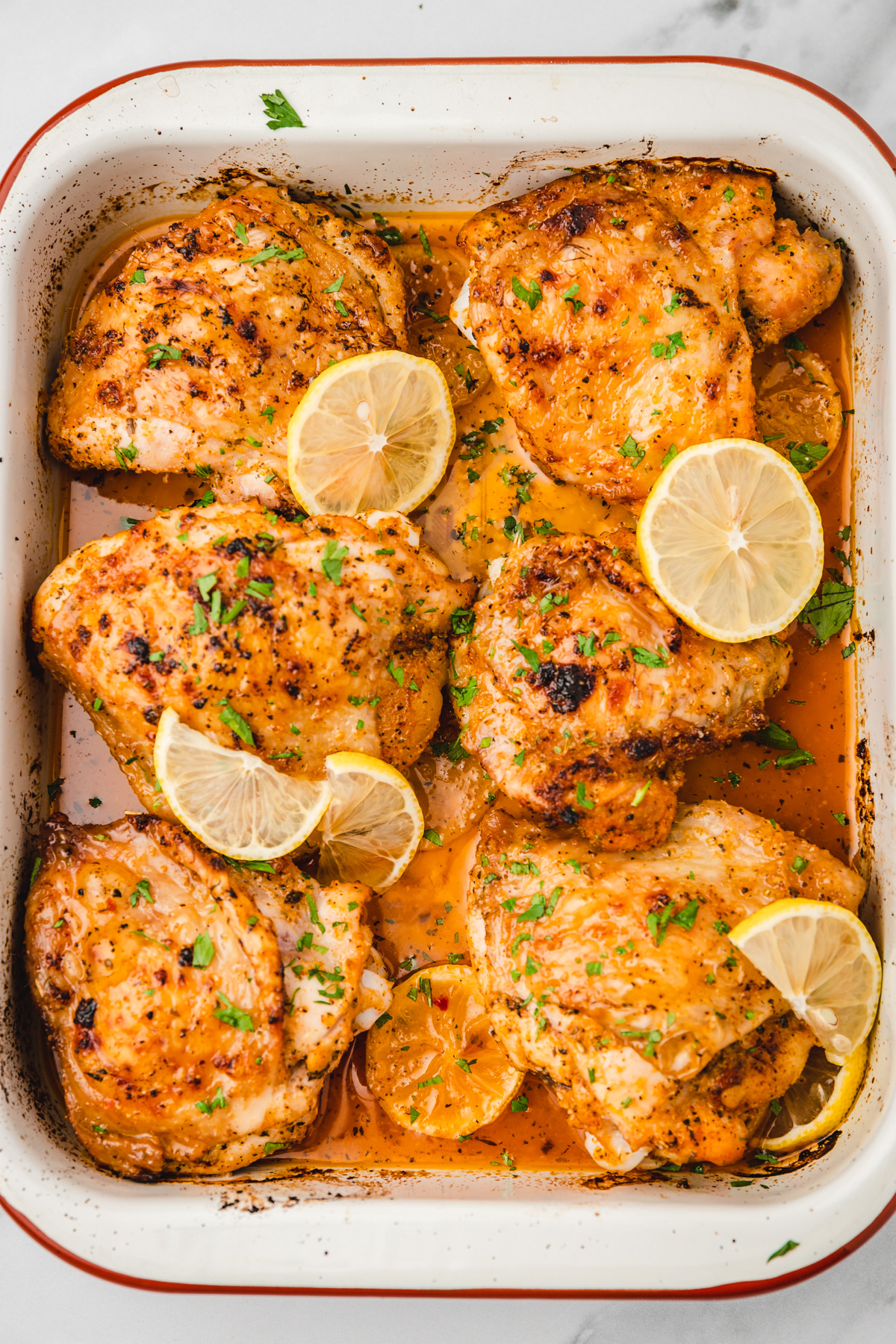 baked chicken with lemon slices in rimmed enamel baking sheet.