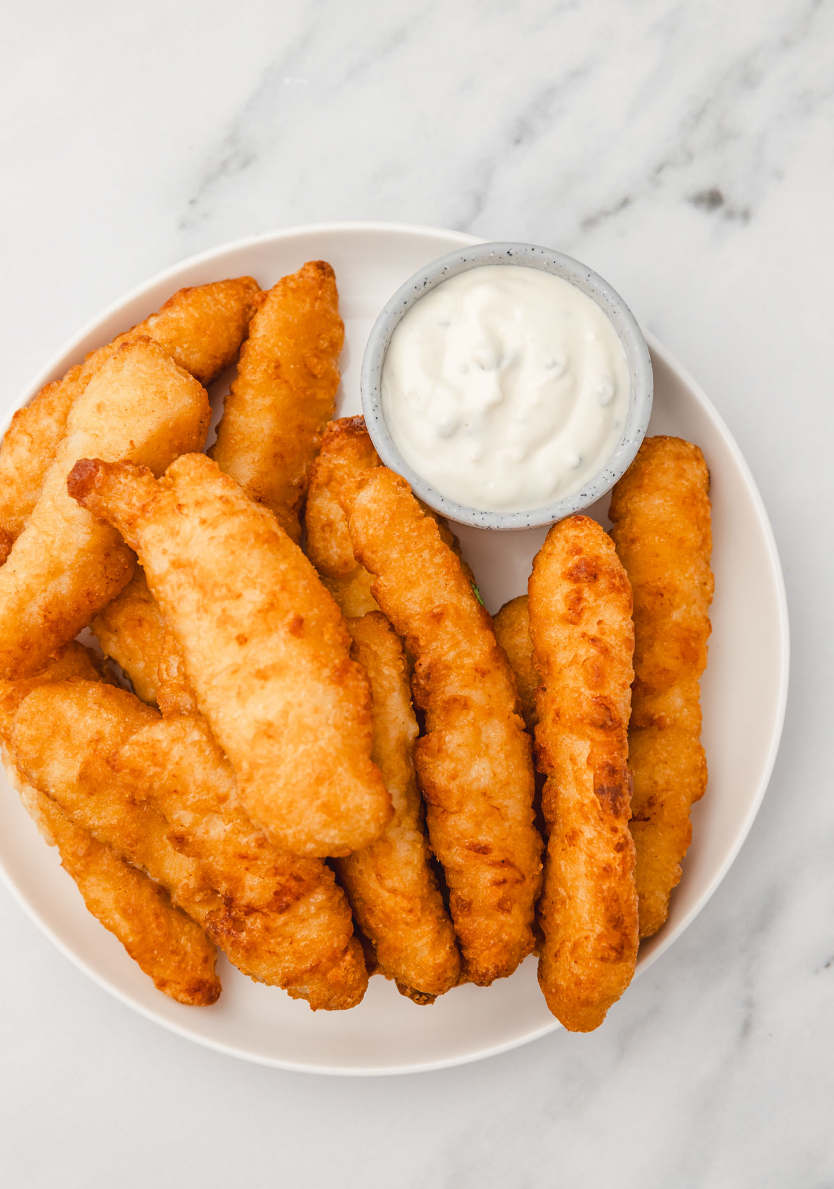 battered chicken strips on a white plate with a small pot dipping sauce.