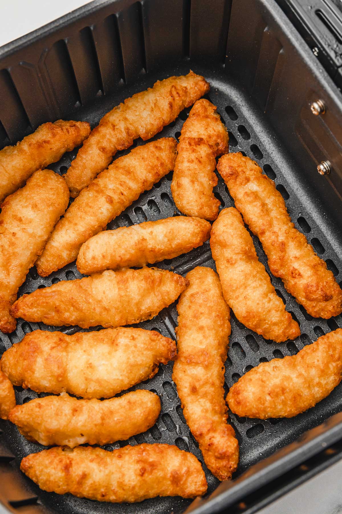 cooked battered chicken strips in the air fryer basket.