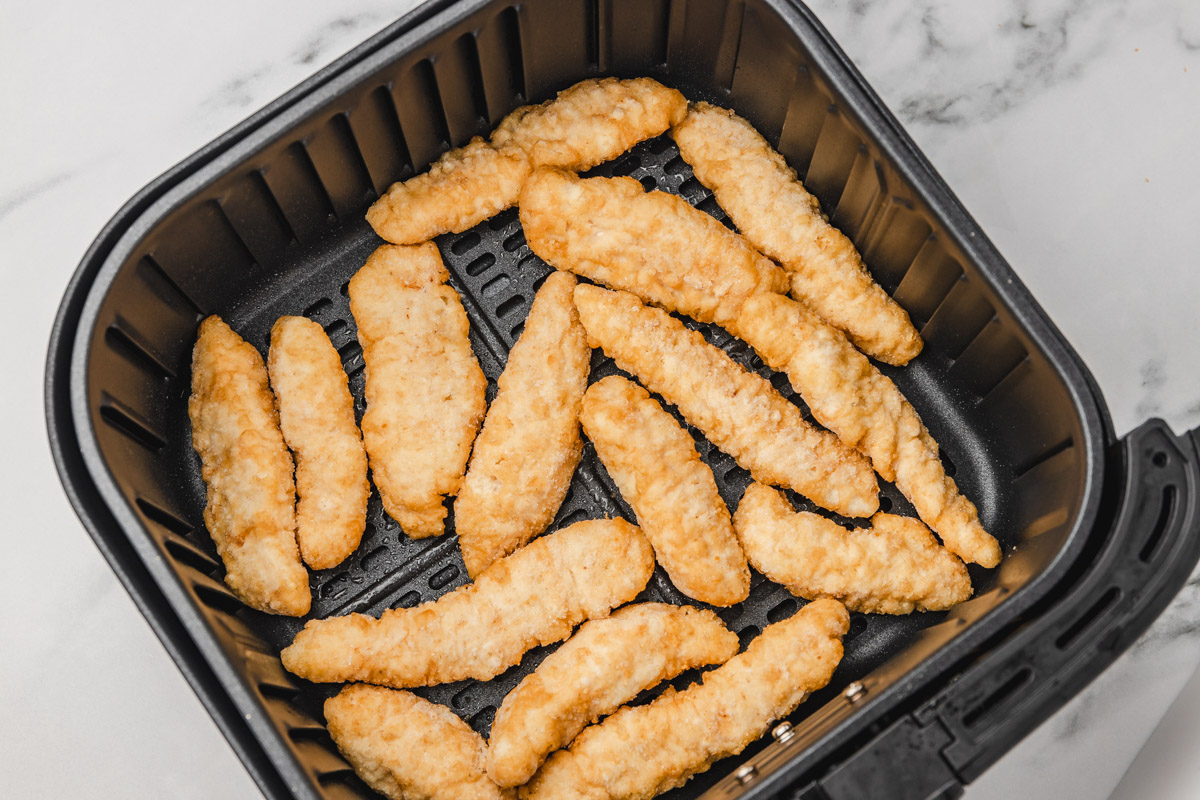 frozen chicken strips in an air fryer basket.
