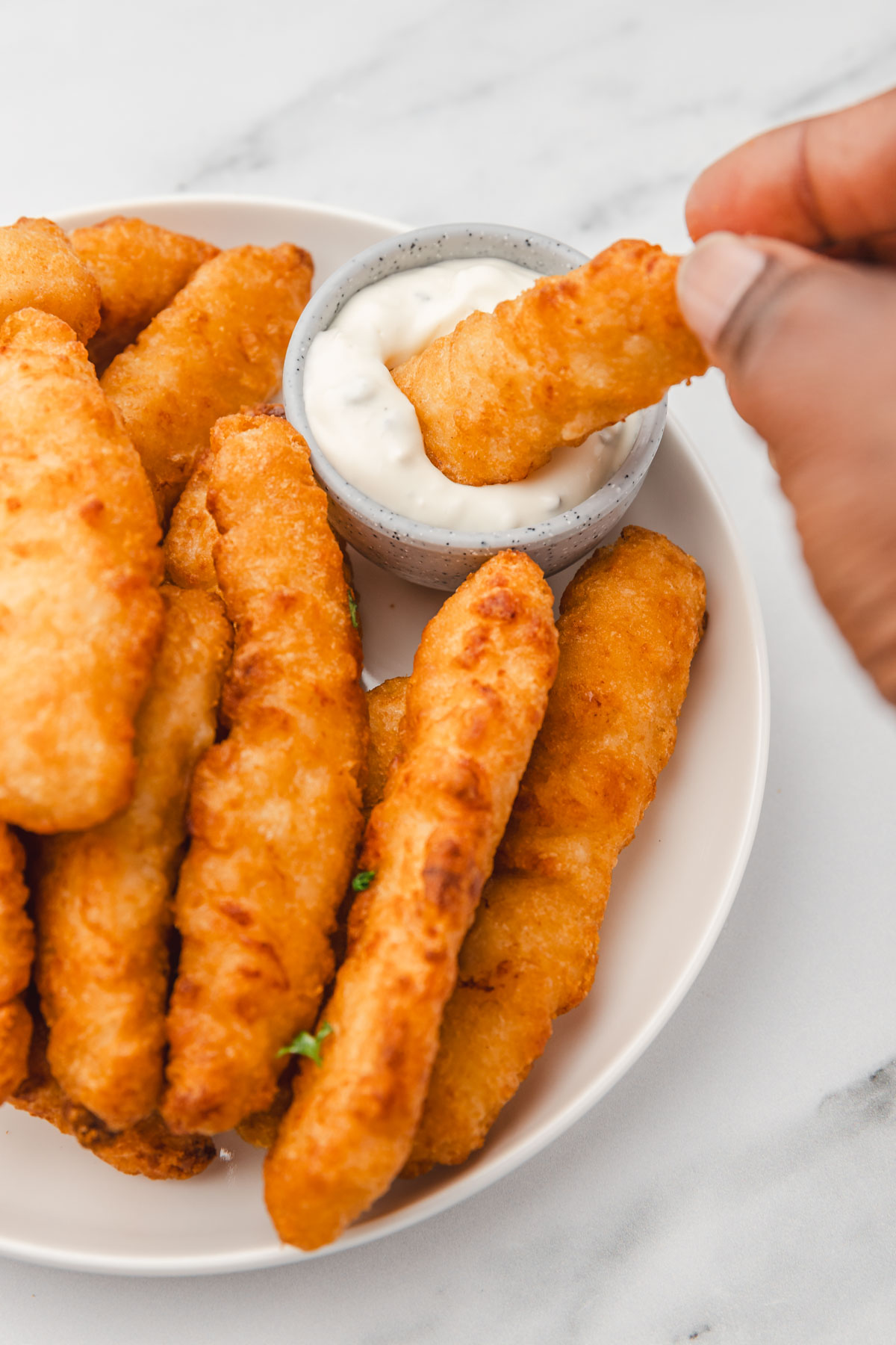 a hand dipping chicken strip in a white dipping sauce.