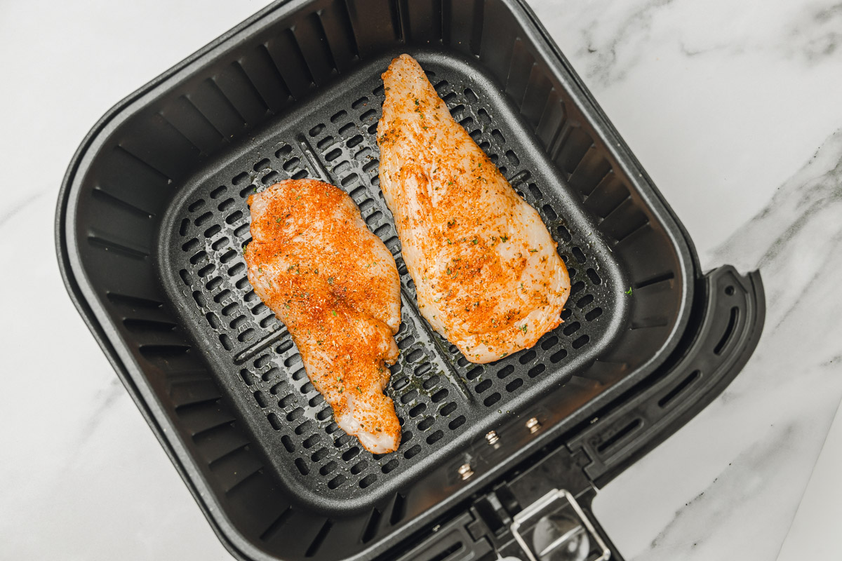 two uncooked chicken slices in an air fryer basket.