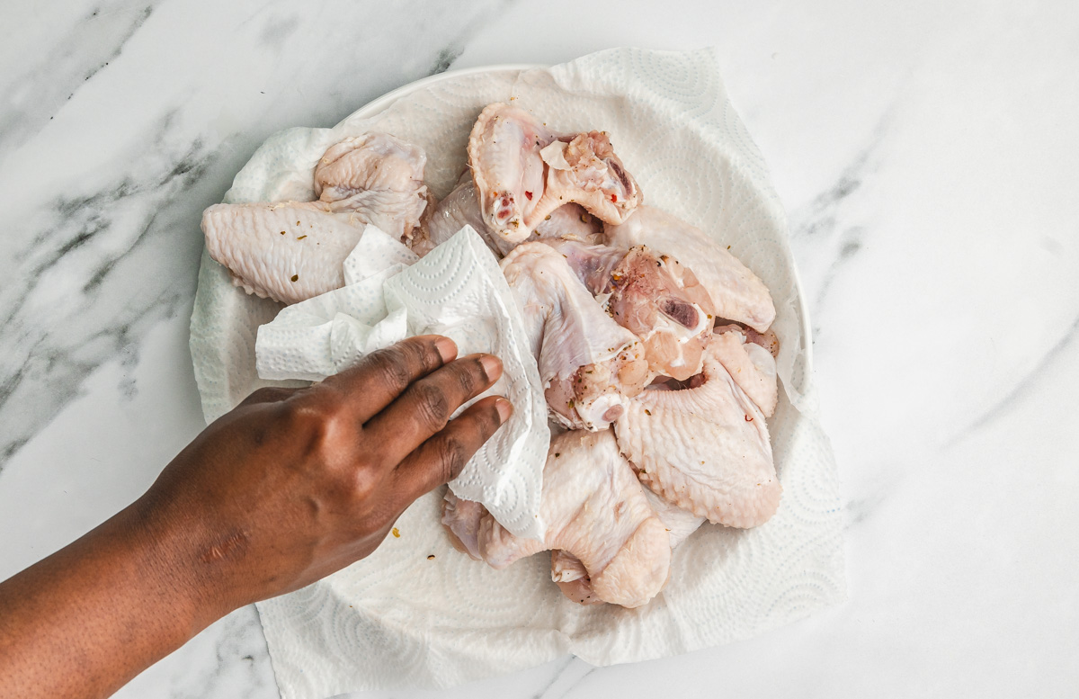 a hand patting chicken wings dry with kitchen paper towel.
