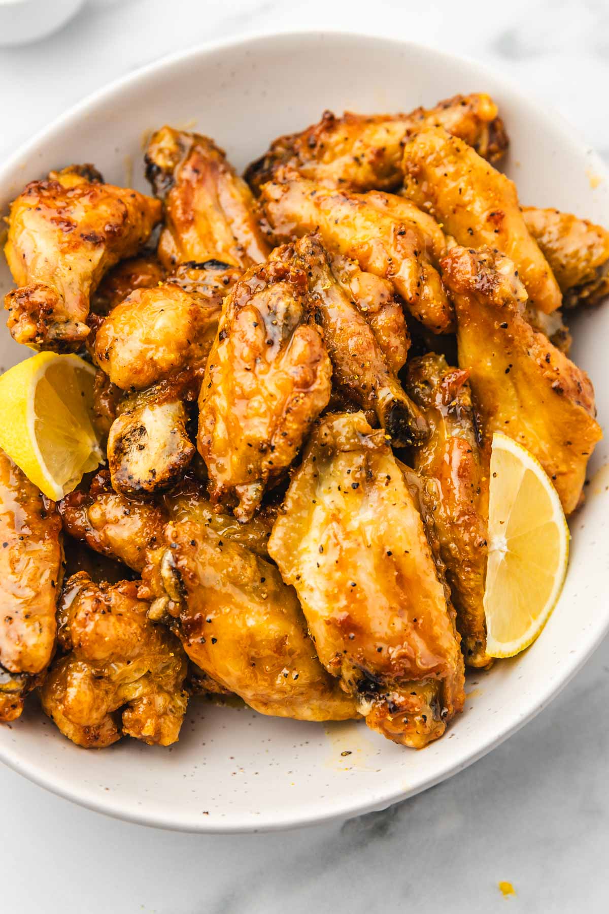 glazed chicken wings on a plate with lemon wedges.