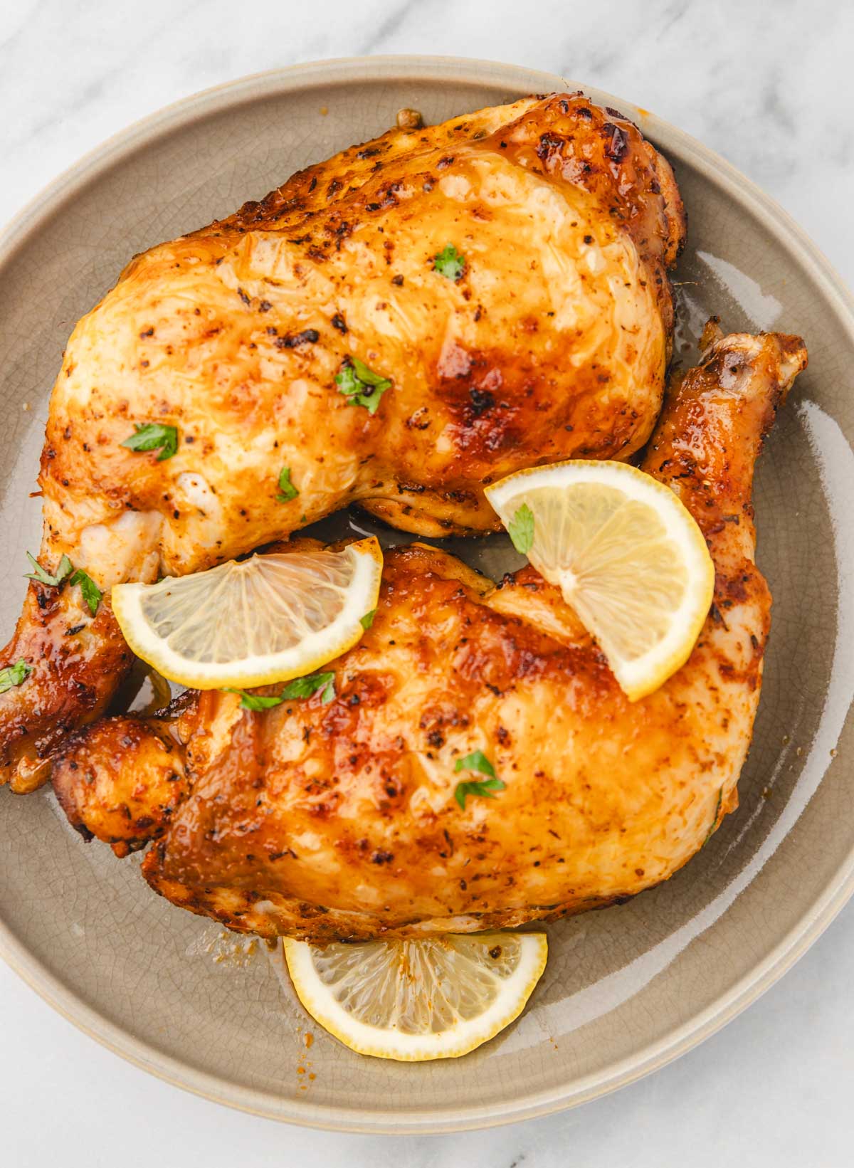 two large whole chicken legs on a plate garnished with lemon slices.