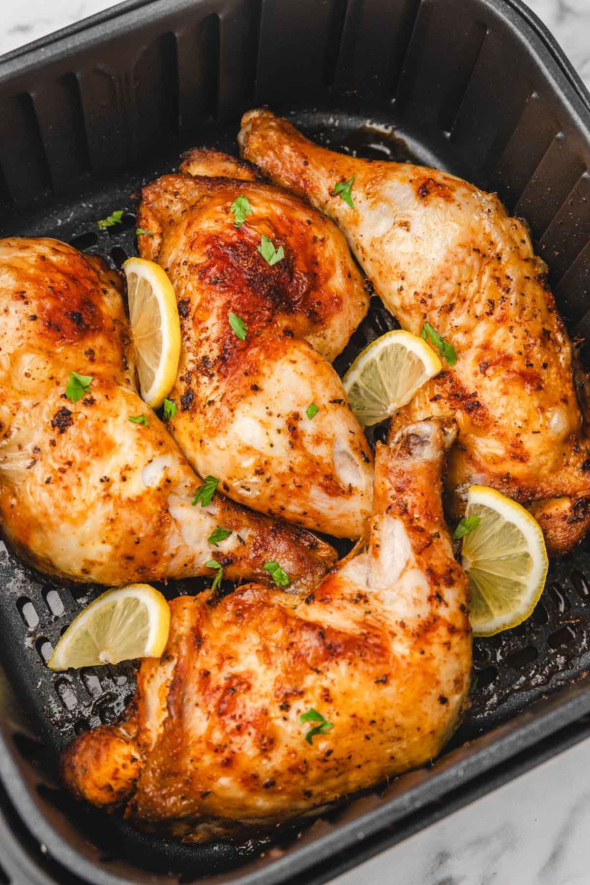 four chicken leg quaters in an air fryer basket.