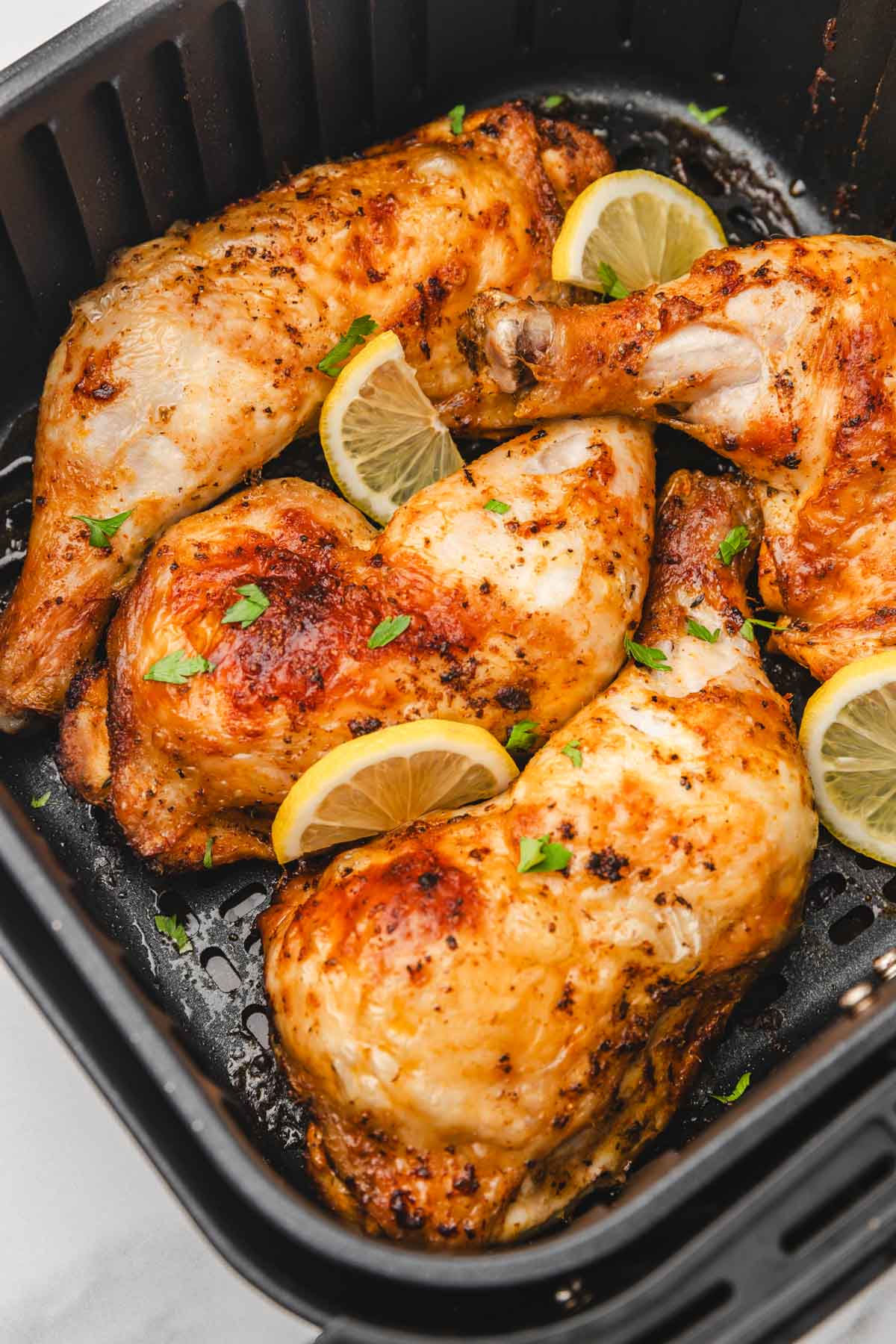 chicken leg quaters in the air fryer garnished with chopped parsley and lemon slices.