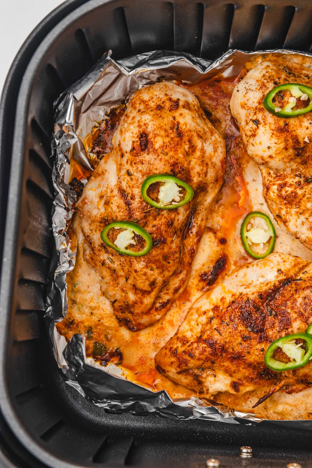 stuffed chicken breasts garnished with sliced jalapeno in air fryer basket.