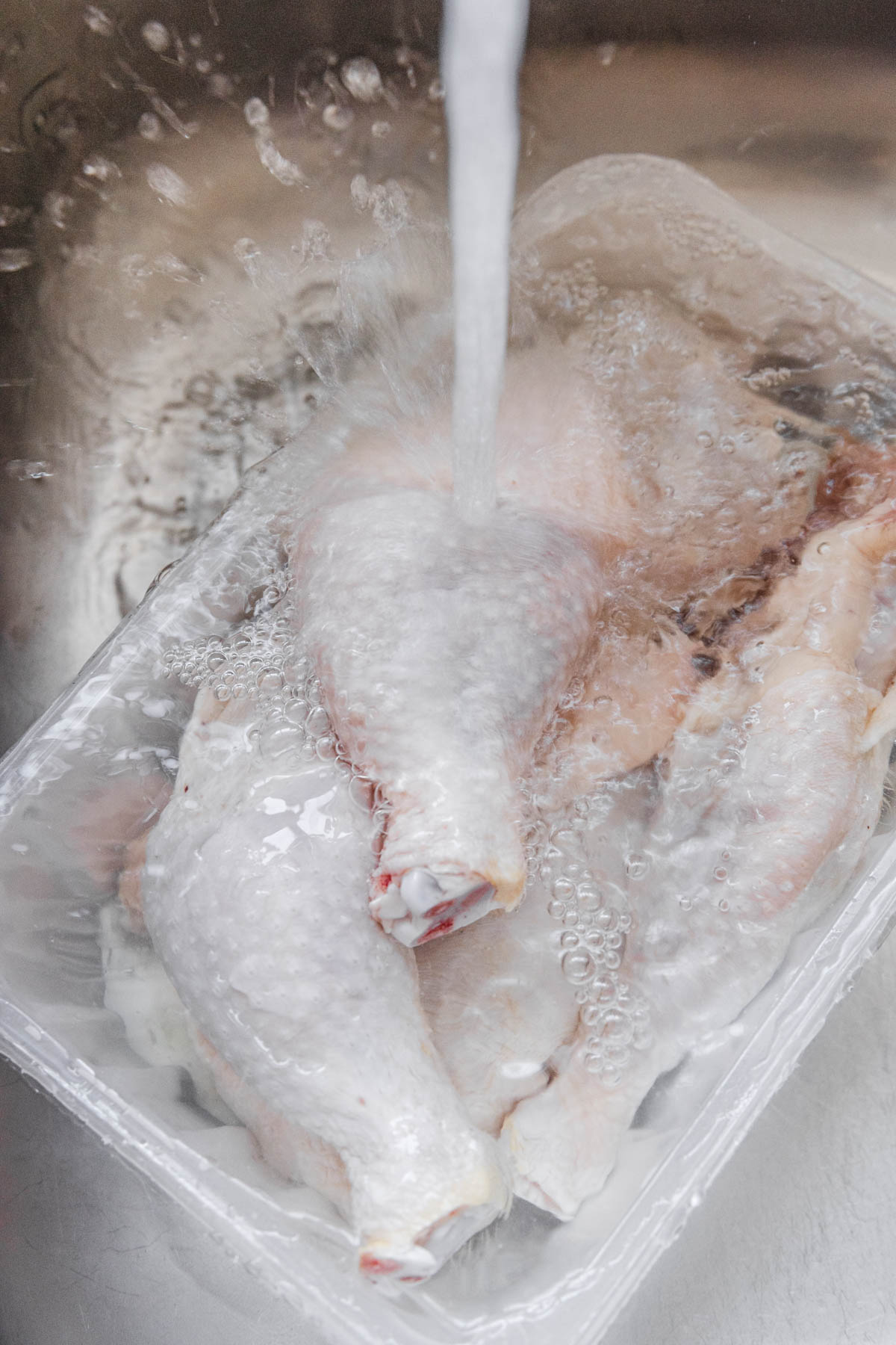 tap and water splaced on chicken leg in a sink.
