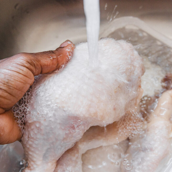 a hand holding chicken leg in rinse under the tap.