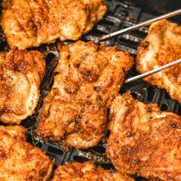 crispy boneless chicken thighs in the air fryer basket with a metal tong.