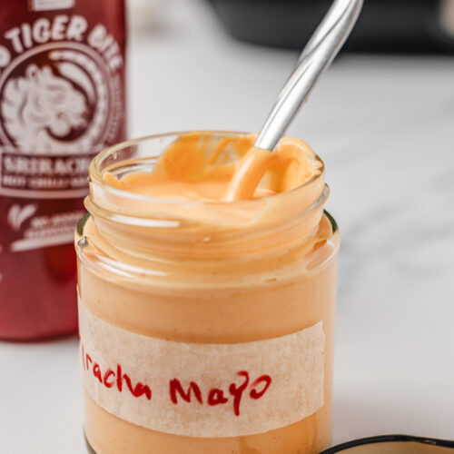 opened sriracha mayo in a jar with a spoon in it.